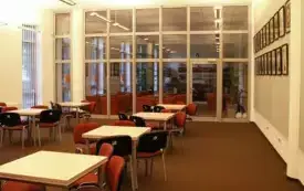 Sala nr 8, ujęcie na salę o szarych ścianach i tylnej szklanej ścianie, na brązowej podłodze stoją stoliki i czerwone krzesła.