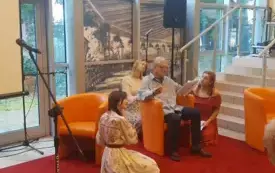 Zbliżenie na Teatr Most&oacute;w podczas czytania performatywnego. Michał Anioł siedzi na pomarańczowym fotelu i odczytuje swoją kwestię, obok niego i za nim na podłodze siedzą Barbara Czubieniak, Natalia Skubiszyńska oraz Klaudia Siewierska. 