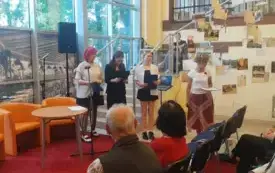 Zbliżenie na czytającą młodzież z grupy Teatralni. Licealiści odczytują utwory Kochanowskiego, obok stoi Aneta Gizińska-Hwozdyk. Z przodu zdjęcia widać część widowni.