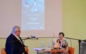 Przy okrągłym stoliku siedzą Zofia Mąkosa i Sławomir Szenwald. Za nimi wyświetlony jest plakat wydarzenia
