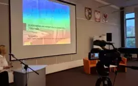 Agata Stępińska-Kaczmarczyk w trakcie przem&oacute;wienia, w centralnym punkcie slajd z prezentacji, z prawej strony kamera