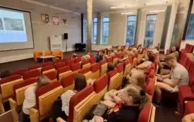 Publiczność zgromadzona w sali audytoryjnej, w tle wykład