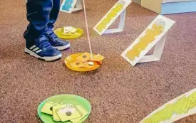 Dziecko za pomocą wędki z magnesikiem odkłada wydrukowane okładki książek na talerzyki w odpowiednich kolorach.