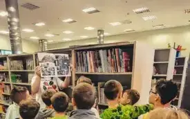 Grupa dzieci przygląda się komiksowi trzymanemu przez bibliotekarkę.
