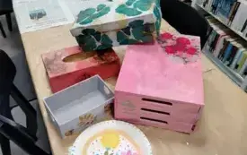 3.	Na stole stoją ozdobne pudełka wykonane podczas zajęć. Największe z nich jest w kolorach r&oacute;żu zmieszanego z niebieskim. Są na nim przyklejone serwetki z czerwonymi r&oacute;żami. Drugie pudełko jest jasne w zielone liście monstery. Trzecije jest szare z motyw