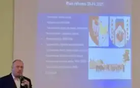 Z lewej strony Roland Semik w trakcie wykładu m&oacute;wi do mikrofonu, za nim slajd z prezentacji multimedialnej