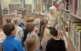 Bibliotekarka oprowadza dzieci po wypożyczalni dla dzieci.