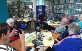 Przy stole siedza osoby uczestniczące w dyskusji. Jedna z os&oacute;b gestykuluje.