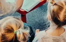 Bibliotekarka czyta dzieciom kartonową książkę z okienkami, zachęcając je do wsp&oacute;lnego odkrywania jesiennych niespodzianek.
