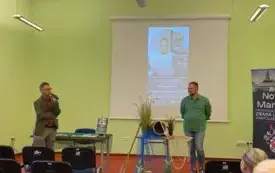 W sali pełnej ludzi Patryk Lewandowski (po lewej) zapowiada Konrada Hamkałę (po prawej). Między nimi stolik z dekoracją przypominającą Odrę. Z boku rollup cyklu spotkań Nowa Marchia