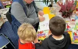 Mężczyzna przy stoliku podpisuje dzieciom książeczki