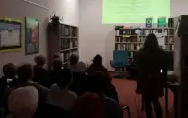 Grupa os&oacute;b uczestnicząca w wydarzeniu promującym Wielkie Litery. W tle prezentacja multimedialna wyświetlana na ścianie.