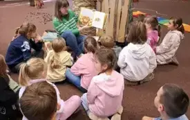 Bibliotekarka czyta dzieciom książkę. Dzieci słuchają. 