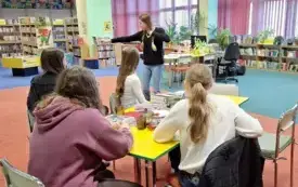 Klubowiczki grają w kalambury. Cztery nastolatki siedzą przy stole, a piąta stoi i pokazuje.