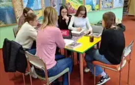 Pięć klubowiczek wraz z moderatorką siedzi przy stole. Dziewczyna w białej bluzce rozpisuje na kartce motyw z książki, reszta uważnie patrzy.