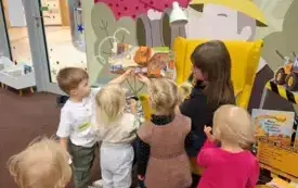 Bibliotekarka czyta książkę &bdquo;Maszyny w akcji&rdquo; Elżbiety W&oacute;jcik. Dzieci poruszają ruchomymi elementami.