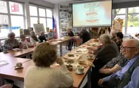 Seniorzy przy stole oglądają prezentację.