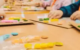 Dzieci siedzą przy stolikach i wykonują zadanie z kolorowymi pomponami.
