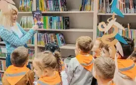 Po lewej bibliotekarka pokazująca książkę z serii Minecraft. Po prawej dzieci.
