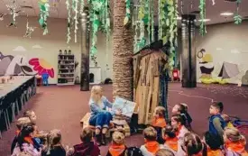 Bibliotekarka czyta książkę uczestnikom lekcji bibliotecznej w Oddziale Dziecięcym.