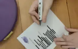 Zbliżenie na leżącą na podłodze kartkę z nowo utworzonym wierszem, nad nią ręka trzymająca flamaster