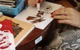 Jedna z uczennic zamalowująca fragmenty i tworząca nowy wiersz siedzi przy stoliku, zbliżenie na dłonie i kartkę z wierszem