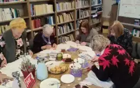 Uczestnicy spotkania DKK przy stole. Wykonują dodatkową pracę - tworzą ozdobne koszulki.