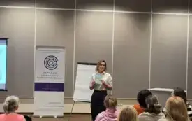 Na zdjęciu widać panią Justynę Bucknall - Hołyńską i siedzących obok niej uczestnik&oacute;w spotkania. Pani Justyna prezentuje  książkę, kt&oacute;ra stała się motywem spotkania.