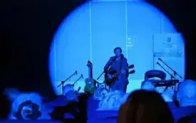 Koncert Limboskiego. Kadr przedstawiający scenę oświetloną niebieskim światłem oraz Limboskiego grającego na gitarze i śpiewającego.