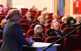 Prof. dr hab. Małgorzata Mikołajczak przemawia do mikrofonu podczas swojego wykładu. W tle widać publiczność siedzącą i słuchającą prelekcji.