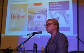 Prof. dr hab. Małgorzata Mikołajczak przemawia do mikrofonu podczas swojego wykładu. W tle widoczny jest ekran z prezentacją.