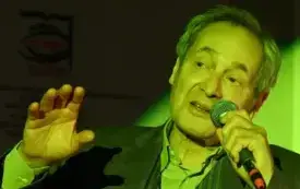 zbliżenie na Jerzego Zelnika, kt&oacute;ry przemawia do mikrofonu i gestykuluje. Na scenę rzucana jest okrągła poświata zielonego światła