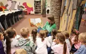 Bibliotekarka czyta dzieciom książkę pod bibliotecznym drzewkiem