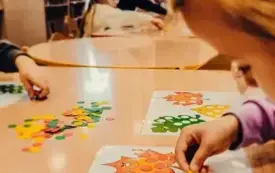 Dzieci przy stolikach wykonują zadanie z jesiennymi liśćmi.