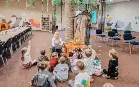 Bibliotekarka rozmawia z grupą dzieci siedzących na podłodze.