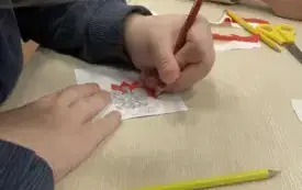 W dłoni nad malowanką czerwona kredka, obok leży ż&oacute;łta kredka.