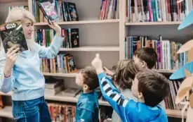 Bibliotekarka pokazuje dzieciom książki o Lego i Minecrafcie. Dzieci wskazują je palcami.