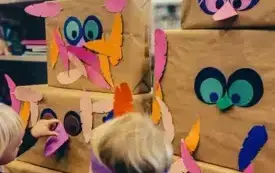Dzieci ozdabiają indiański totem za pomocą pi&oacute;rek z kolorowego papieru.