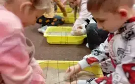 Dzieci sięgają do pojemnik&oacute;w wypełnionych piaskiem i wyciągają ukryte obrazki z r&oacute;żnymi narzędziami budowlanymi.