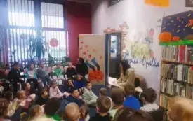 Grupa dzieci siedzi na dywanie przed kobietą na krześle czytającą bajkę.