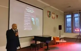 Prof. Arkadiusz Słabig w trakcie wystąpienia, za nim plakat wydarzenia i fortepian