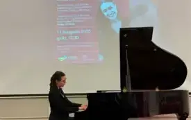 Lena Juszkiewicz przy fortepianie, za nią wyświetlony plakat wydarzenia