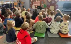 Dzieci siedzą na dywanie, prowadzącą czyta tekst i pokazuje obrazki.