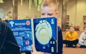 Bibliotekarka pokazuje dzieciom ilustracje w książce podczas spotkania Dyskusyjnego Klubu Książki.