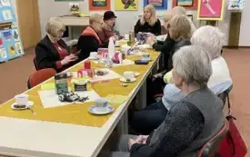 Przy długim stole siedzi 9 dorosłych os&oacute;b, w tle dziecięca wystawa.