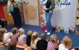 Dwie kobiety stoją przed grupą dzieci siedzących na dywanie