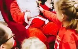 Dziewczynka wyciąga rękę po dzwonek Świętego Mikołaja. 