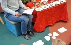 Druga bibliotekarka czyta toruńską legendę, tłumacząc skąd się wziął kształt katarzynek. Na podłodze leżą szablony piernik&oacute;w.