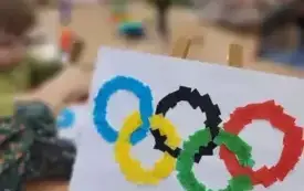 Flaga olimpijska z bibuły. W tle dzieci wykonujący tę pracę plastyczną. 