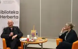 Robert Rudiak oraz Agnieszka Kopaczyńska-Moskaluk siedzą przy udekorowanym stoliku na tle baneru Biblioteki Herberta i rozmawiają o tomiku "Seans spirytystyczny".